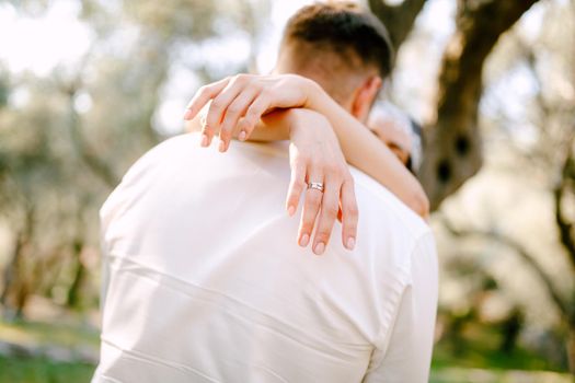 The bride gently hugs the groom in the park, wrapping her arms around his neck, close-up . High quality photo