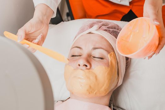 Woman at the beautician applying a relaxing golden mask on the face, restoring and moisturizing the skin. new
