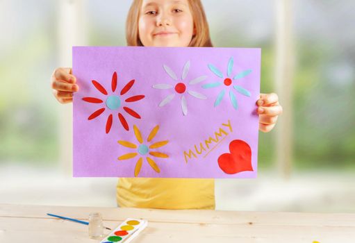 Happy little girl is showing greeting card for mothers day, focus on card