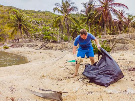 Man in gloves pick up plastic bags that pollute sea. Problem of spilled rubbish trash garbage on the beach sand caused by man-made pollution and environmental, campaign to clean volunteer in concept.