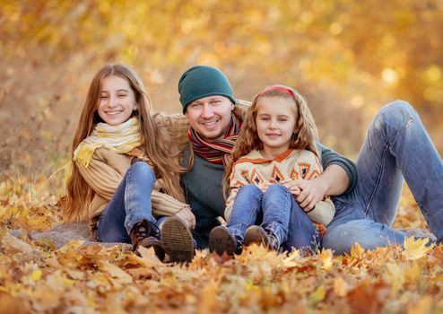 Daughters and father sitting in autumn leaves