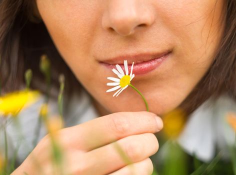 A woman is holding a daisy near face, close-up