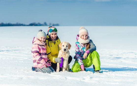 Happy mother and daughters walking ouside with dog in winter