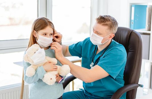 Kind doctor putting medical mask on little girl in clinic