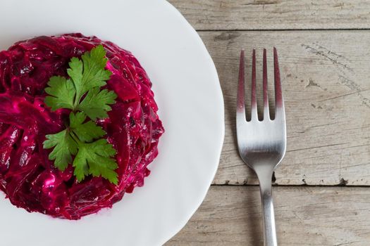 Beet salad with parsley on a white plate on a wooden table, top view