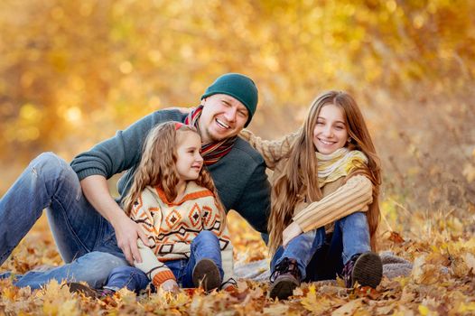 Daughters and father sitting in autumn leaves