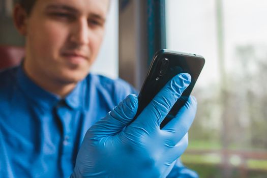 A guy in protective medical glove hold a phone and spends time in it, close-up.