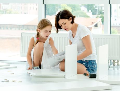 Adorable kid girl helping mother in installing brand new bookshelf