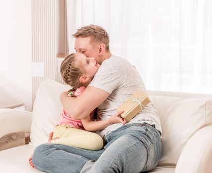 Loving daughter surprise dad with Fathers day gift and a sincere embrace