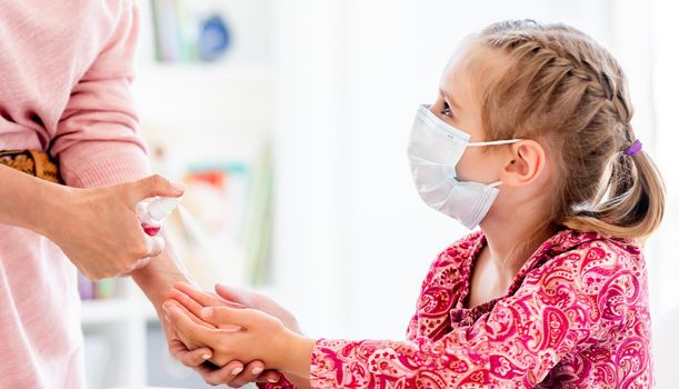 Teacher spraying sanitizer on little girl's hands at school during quarantine