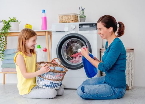 Happy mother and little daughter washing clothes using machine in light room