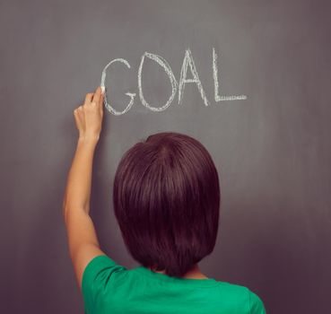 Unrecognizable woman writes the word goal on the blackboard, rear view