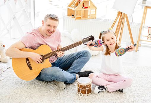 Smiling father and little daughter playing musical instruments in kids room