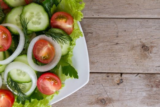 Fresh salad from vegetables, herbs, on a wooden table, top view. Space for text