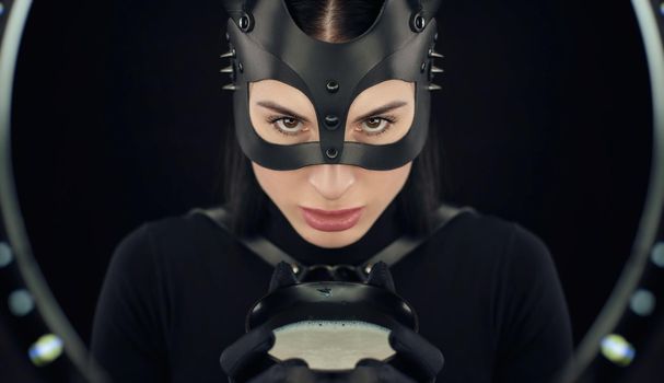 the woman in a black body belt and cat mask with a bowl of milk