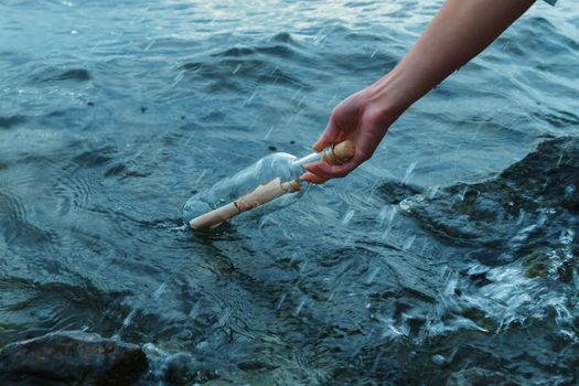 The female hand takes out bottle with a letter for help from sea