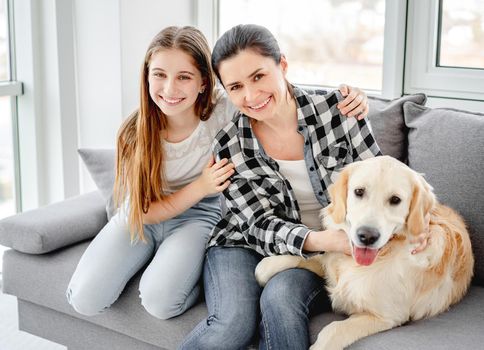 Happy daughter and mother sitting on sofa next to lovely dog