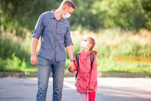 School girl with father in medical masks going back to school