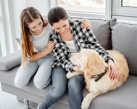 Happy daughter and mother sitting on sofa next to lovely dog