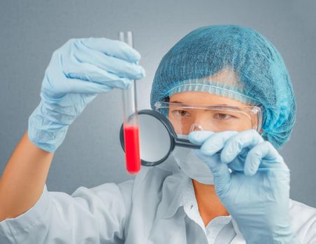 Female scientist looking at a test tube with red liquid through a magnifying glass