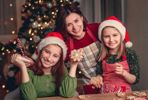 Smiling mother with daughters baking gingerbread near christmas tree at home