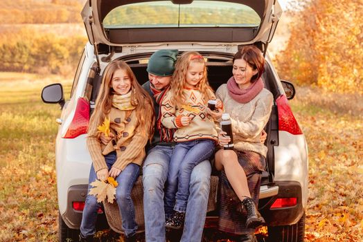 Happy family sitting in car trunk on autumn background