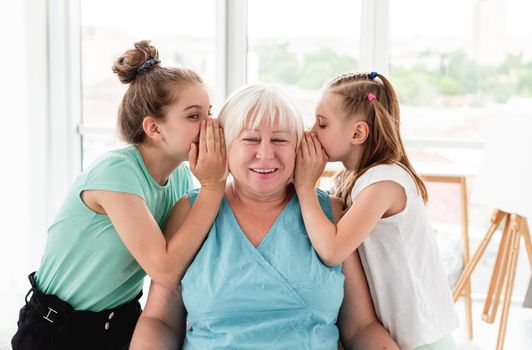 Cute granddaughters sharing secret with grandmother in light room
