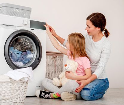 Mother teaching daughter how to operate washing machine in light bathroom