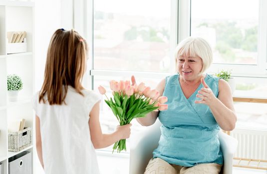 Little girl giving flowers to happy senior woman in light room