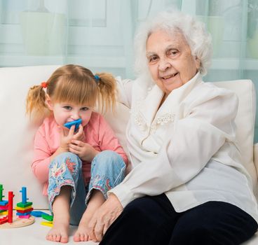 little girl with grandmother sitting on a sofa with toys
