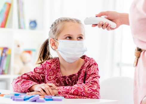 Measuring little girl's temperature with infrared thermometer during pandemic at school