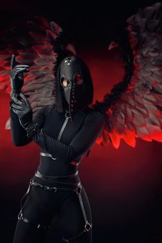 the woman wearing a plague doctor mask with leather straps and black wings on a dark red background