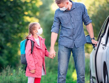 Schoolgirl with father in medical masks getting in car after classes