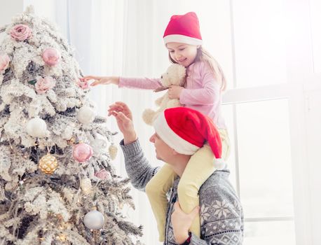 Smiling father in santa hat holding daughter near christmas tree