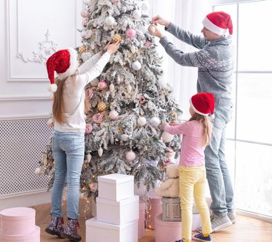 Father and daughters in santa hats decorating christmas tree