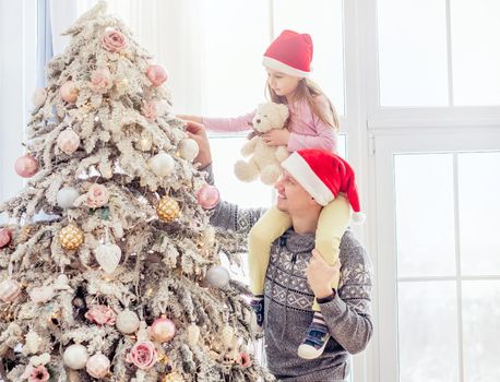 Smiling father in santa hat holding daughter near christmas tree