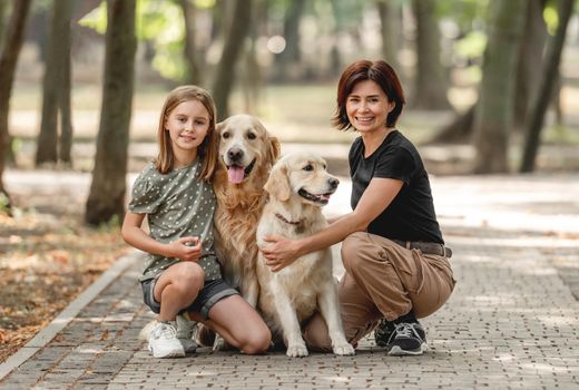 Mother and daughter with golden retriever dogs in the park. Family with pets doggies and preteen girl child outdoors