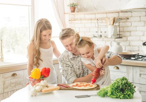 dad with two little daughters preparing pizza in the kitchen