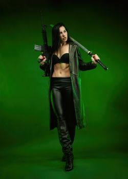 the slender woman in a black leather raincoat with an American automatic rifle and a katana on a green background