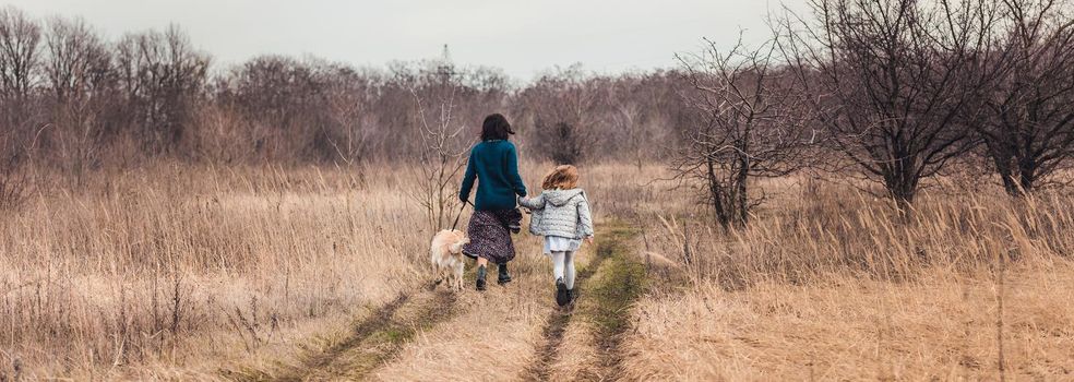 Mother and daughter walking dog along dirt road