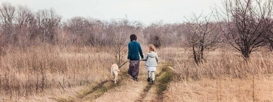 Mother and daughter walking dog along dirt road