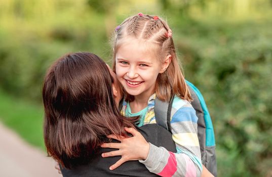 School girl hugging mother after classes in sunny park