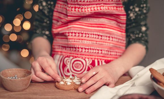 Girl in festive apron decorating gingerbread heart at home