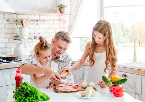 dad with two little daughters preparing pizza in the kitchen