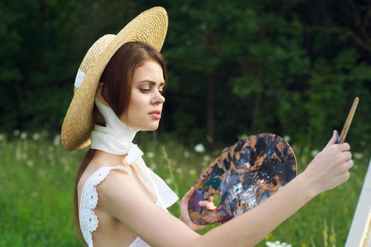 woman with a palette of paints painting a picture outdoors close-up. High quality photo