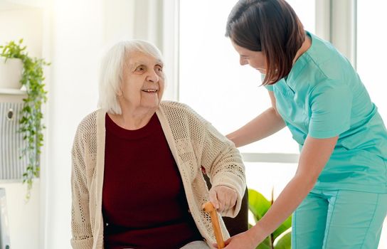 Nurse giving cane to old woman living in home for elderly