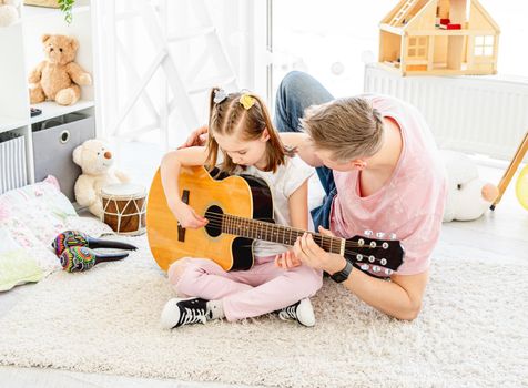 Smiling daughter with father playing guitar at home