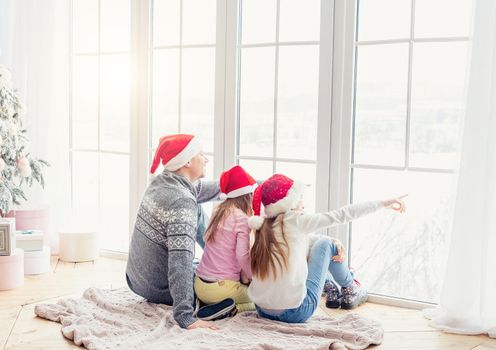 Father and daughters in santa hats sit together looking outdoor