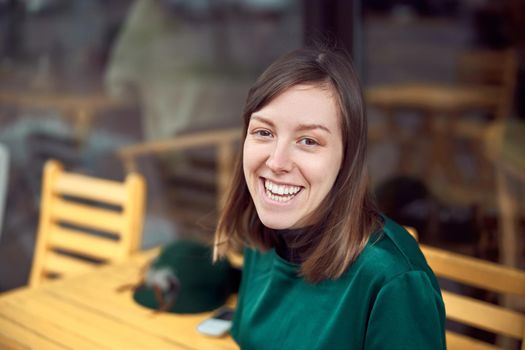 Portrait of cheerful young caucasian woman in green clothes that sitting outside cafe