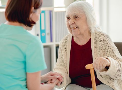 Old lady talking to caregiver holding hands in nursing home